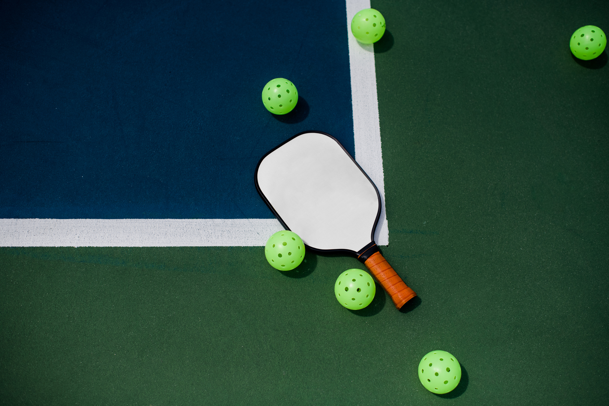 a paddle and six pickleballs lying down on a court 